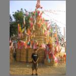 A tall sand chedi with banners near a temple